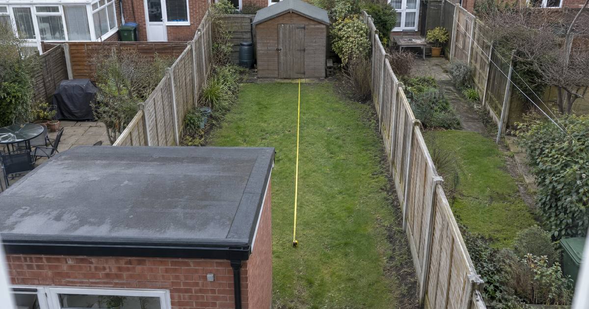 Een smalle achtertuin van bovenaf, met een uitbouw met plat dak tegen het huis, een schuurtje achterin en een meetlint over het gras. Illustratie.