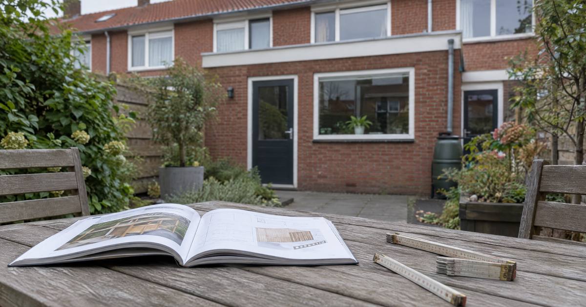 Een opengeslagen klusboek en een duimstok op een houten tuintafel, voor de achtergevel van een rijtjeshuis met een uitbouw. Illustratie.